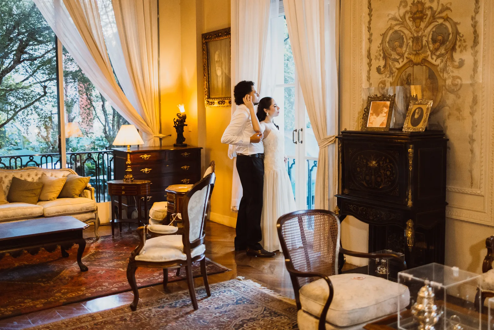 Casal em uma sala de época com cortinas claras e móveis antigos, na Casa da Don’Anna