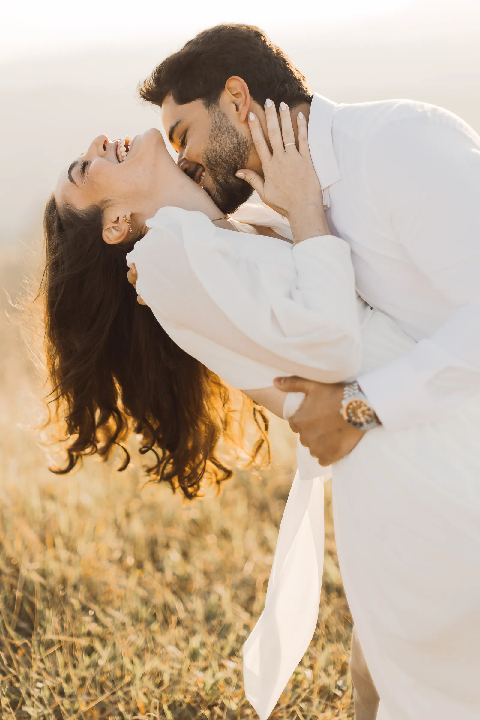 Groom kissing the bride at sunset in a field of tall grass