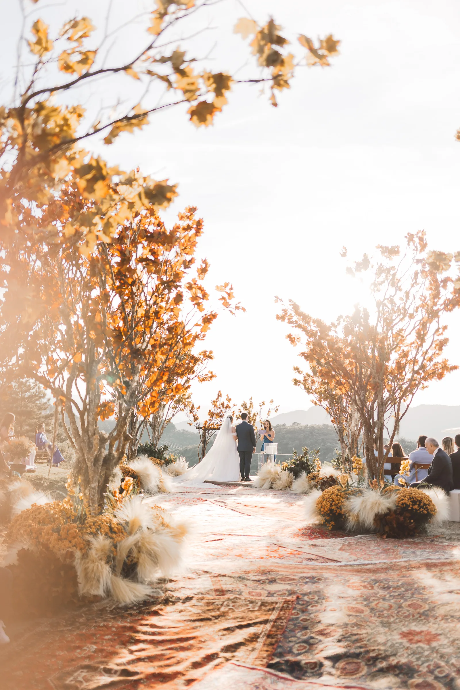 Outdoor ceremony with dry-leaved trees and rugs lining the aisle to the altar