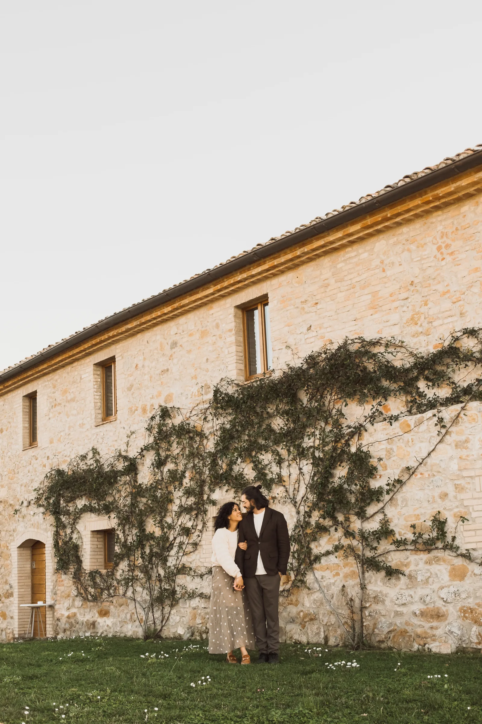 Couple embracing in front of a stone house covered in climbing vines